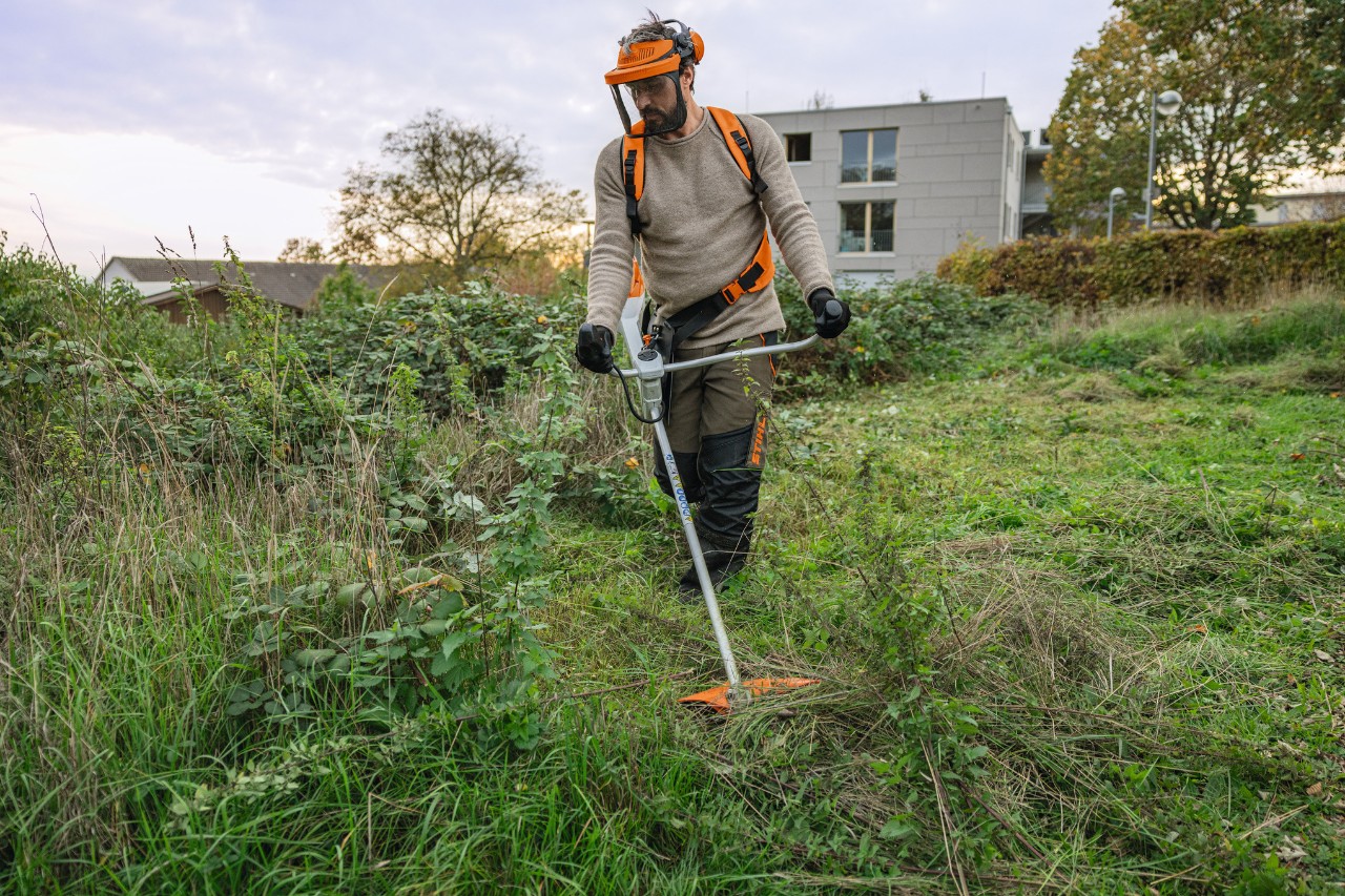 A man wearing STIHL protective equipment mows a wild and overgrown green area using a STIHL FSA 200 cordless clearing saw
