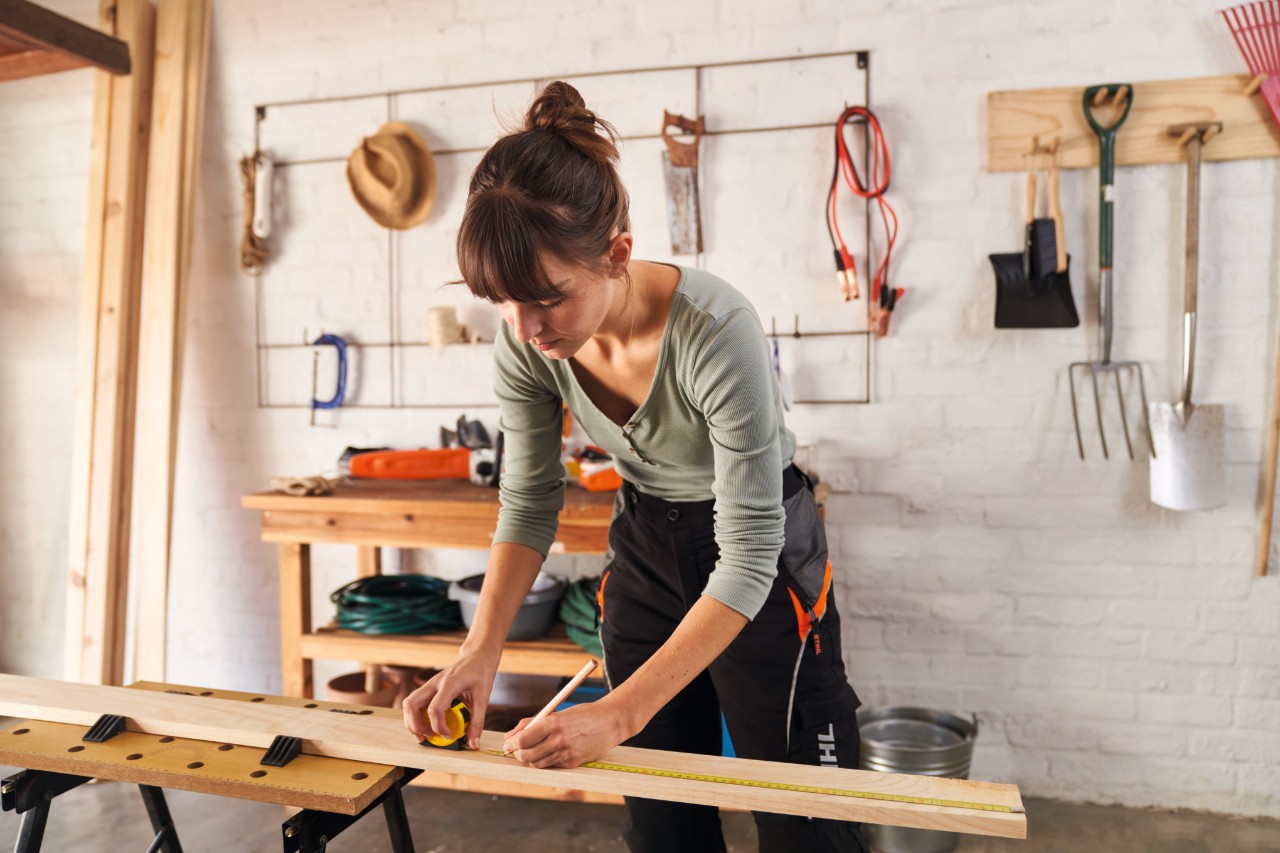 Woman measuring wooden parts on workbench with a measuring tape and marking lengths with a pencil