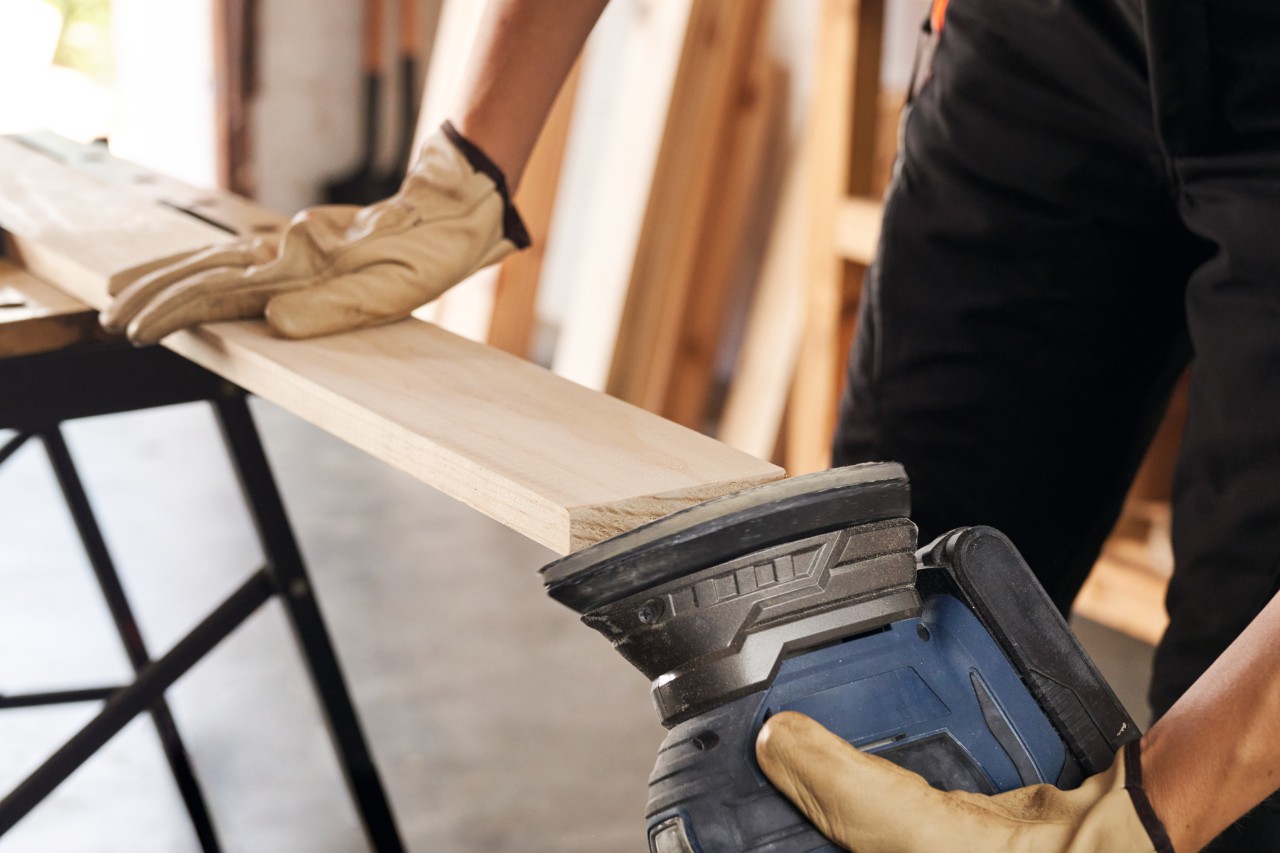 Close-up of a woman using a cordless grinder sanding wooden parts