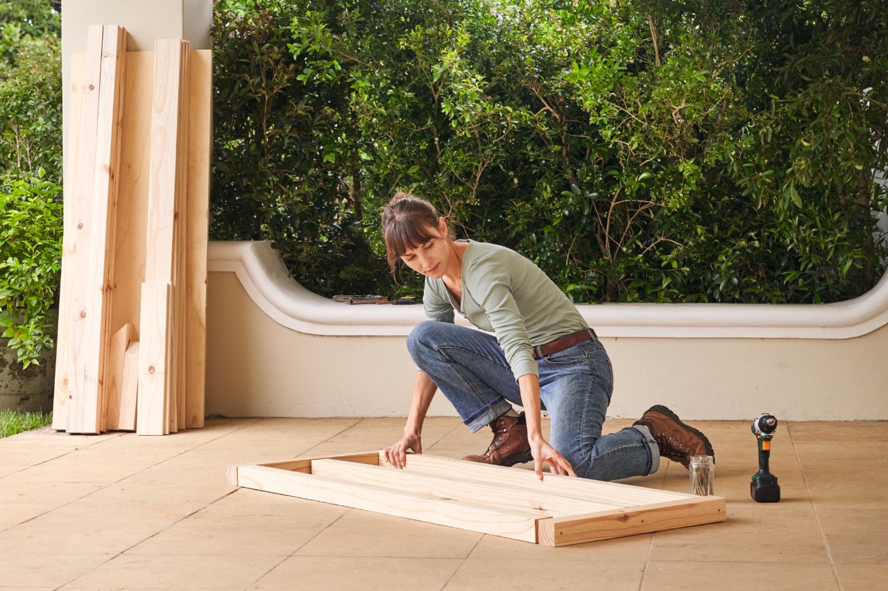 Woman placing the wooden parts for the lower roof structure on a terrace