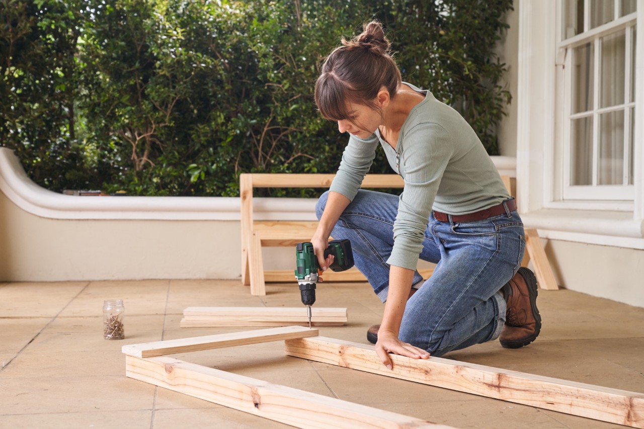 Woman screwing wooden parts together to assemble the side of the tomato house