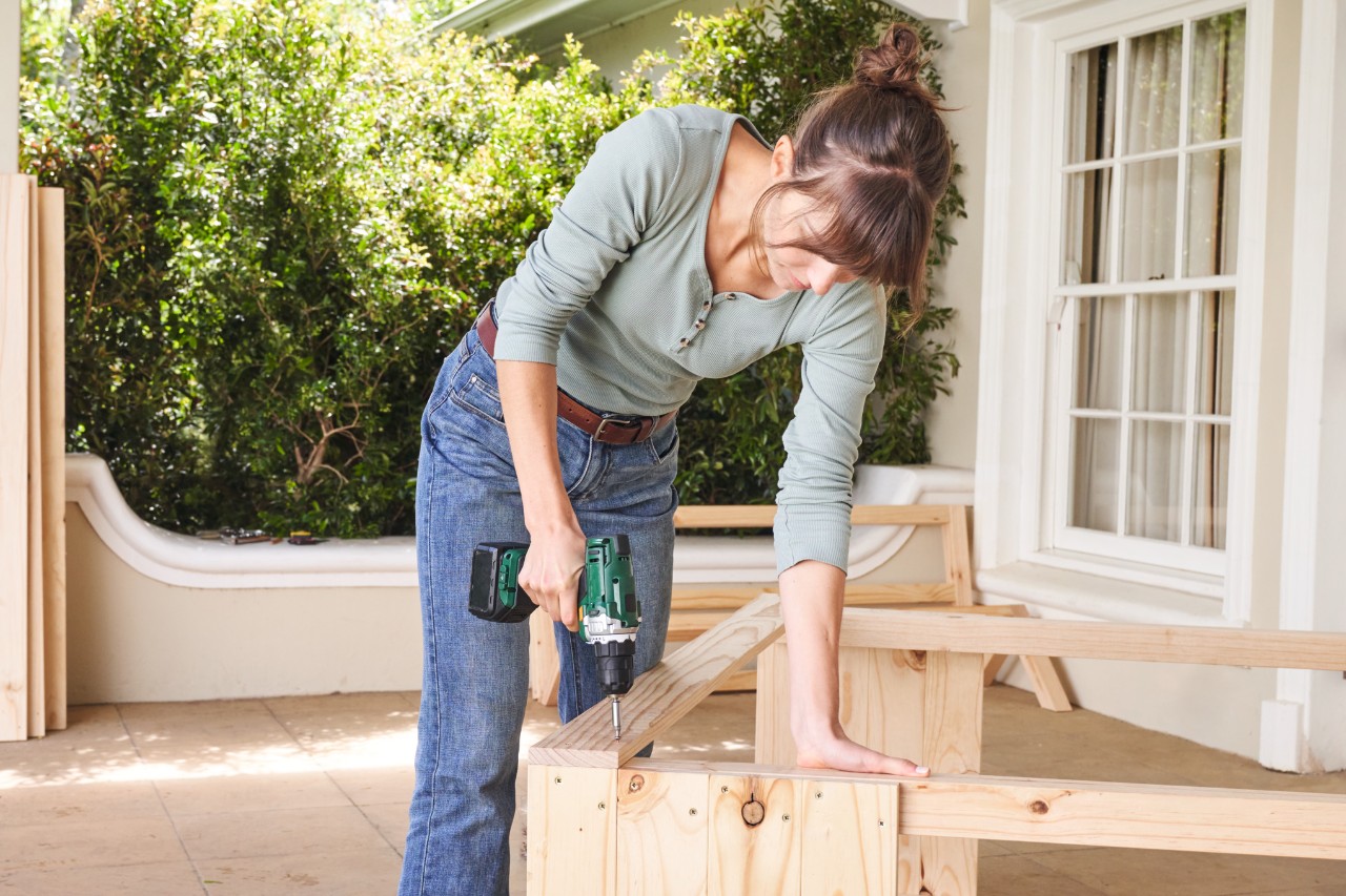 Woman on a terrace screws slats tightly so that they join to form the side panels of the tomato house