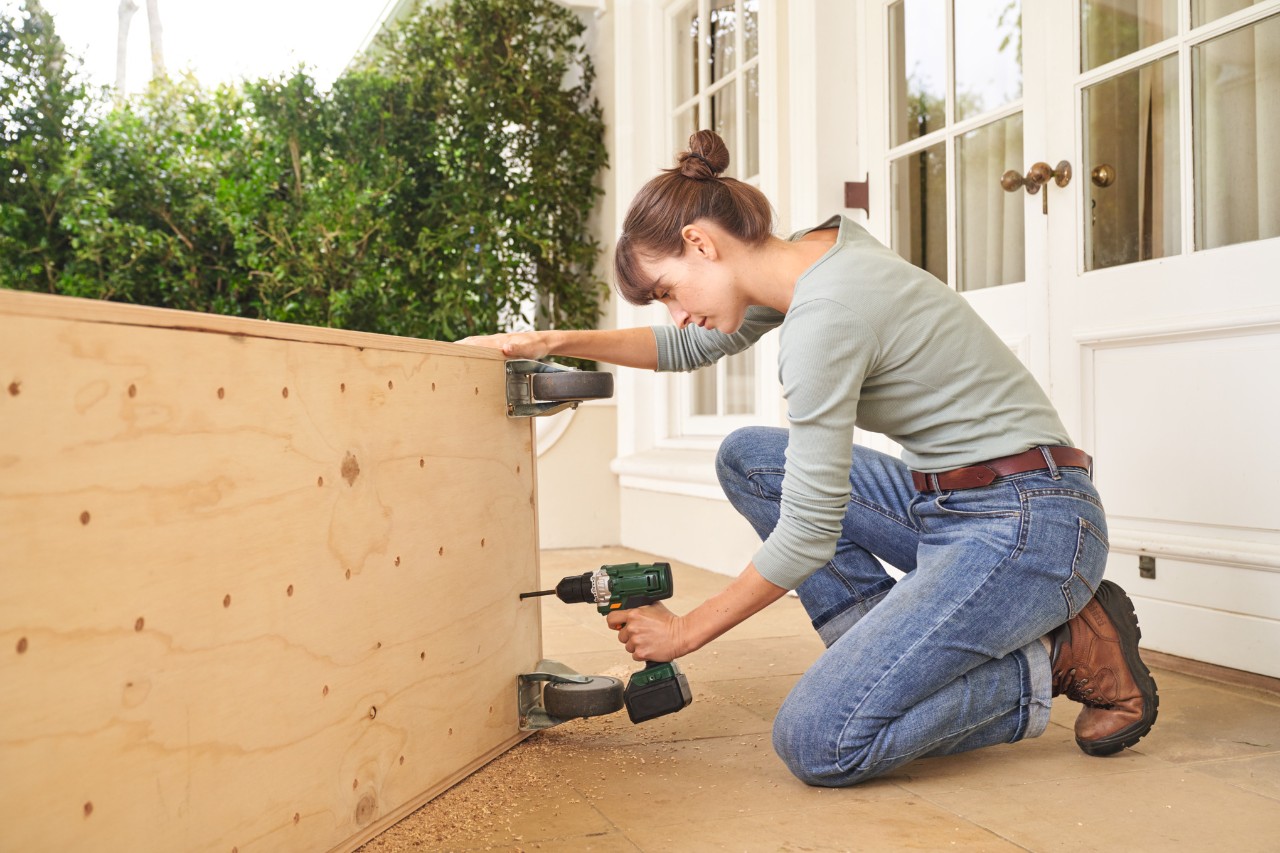 Woman on a terrace floor drilling drainage holes in the floor boards of the tomato house