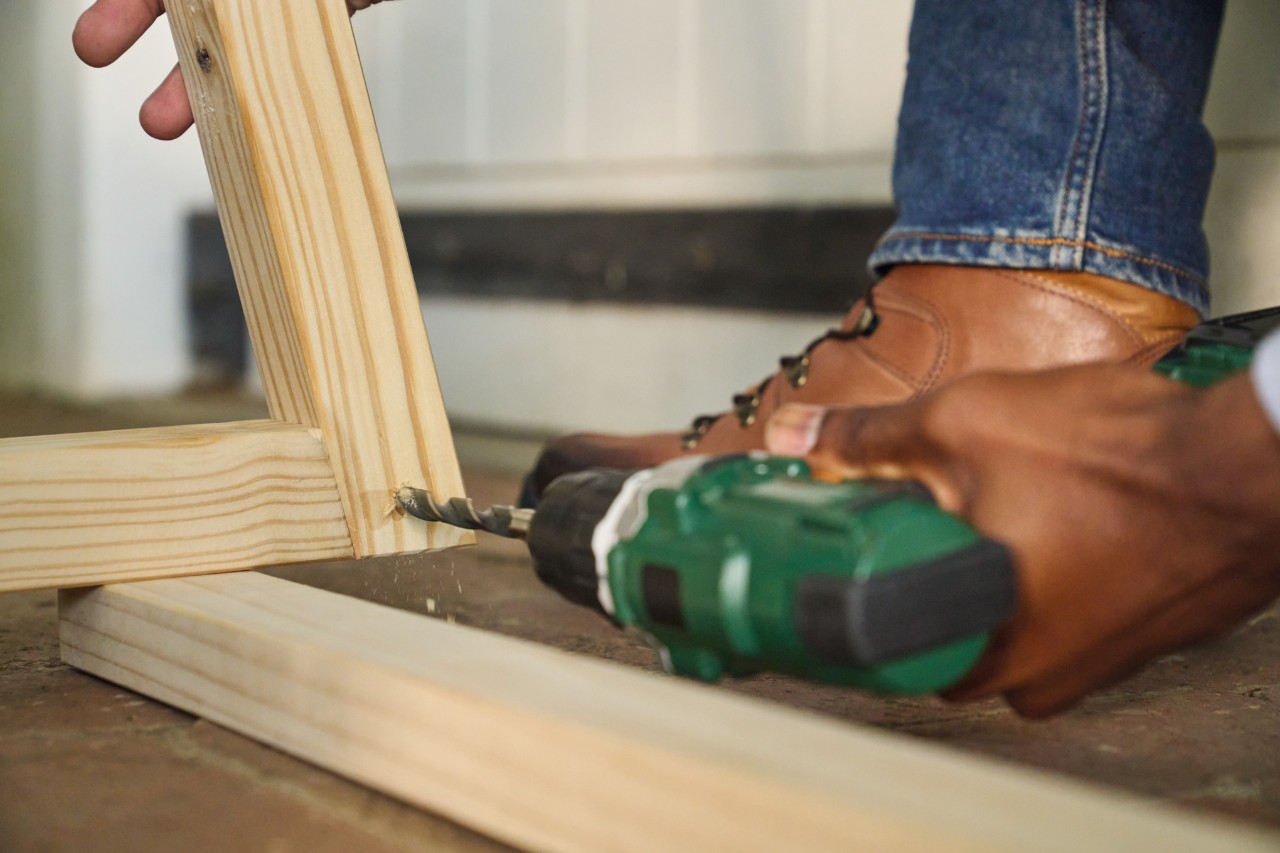 A man drilling holes for the floor strut with a cordless screwdriver