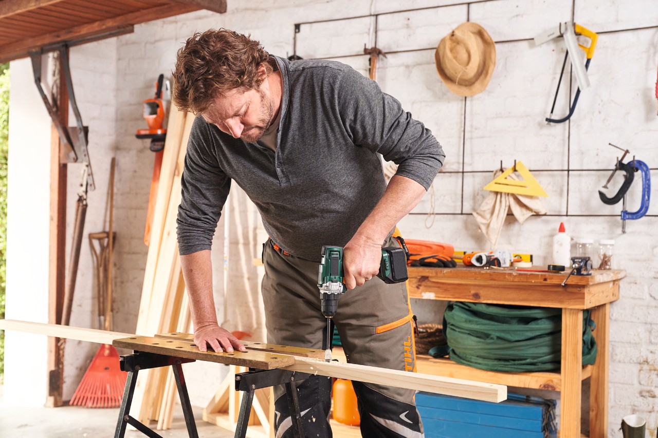A man building a wooden privacy screen in his garage and drills holes in the frame wood
