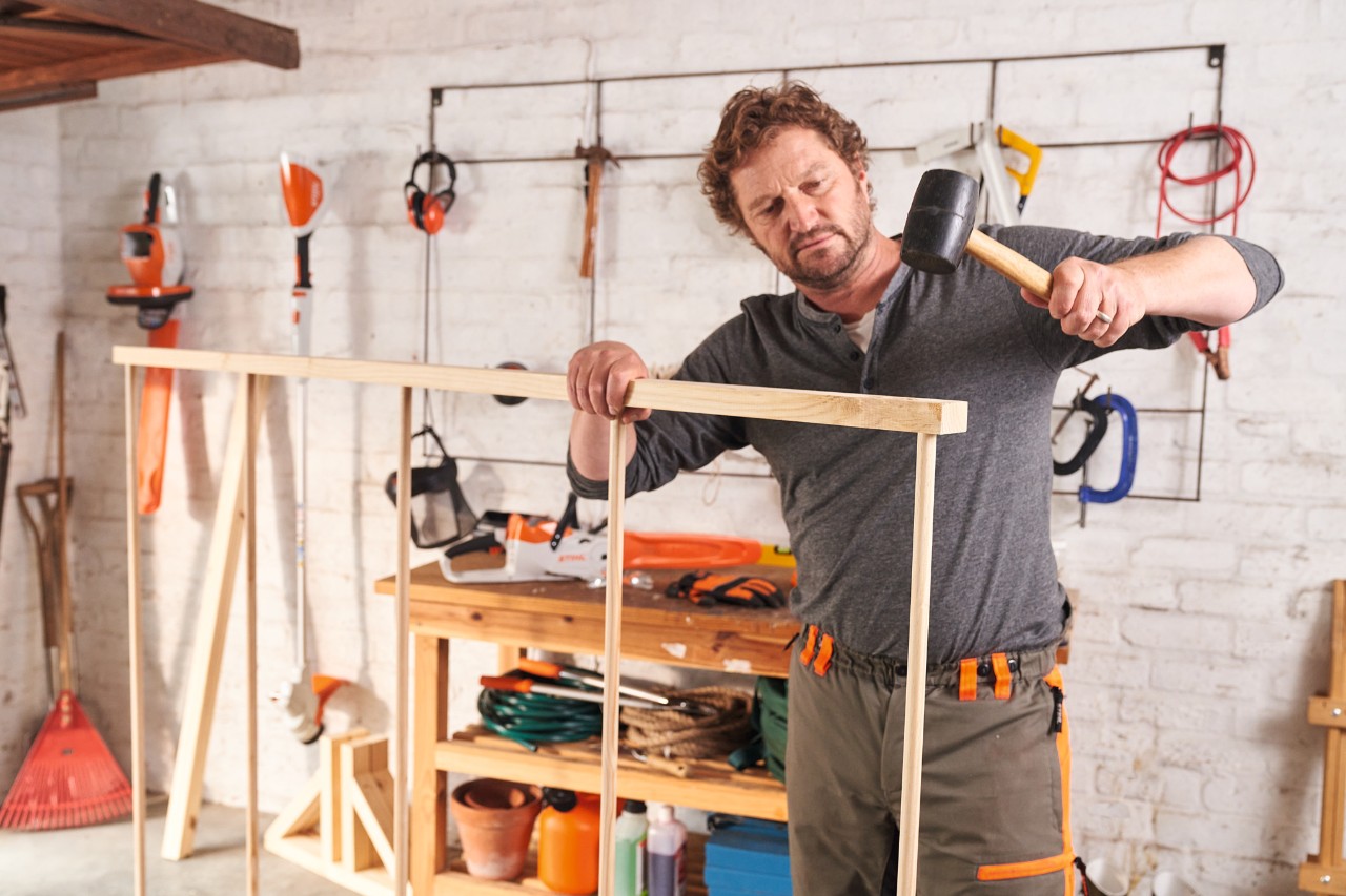 A man building a DIY wooden privacy screen himself and connecting the frame pieces