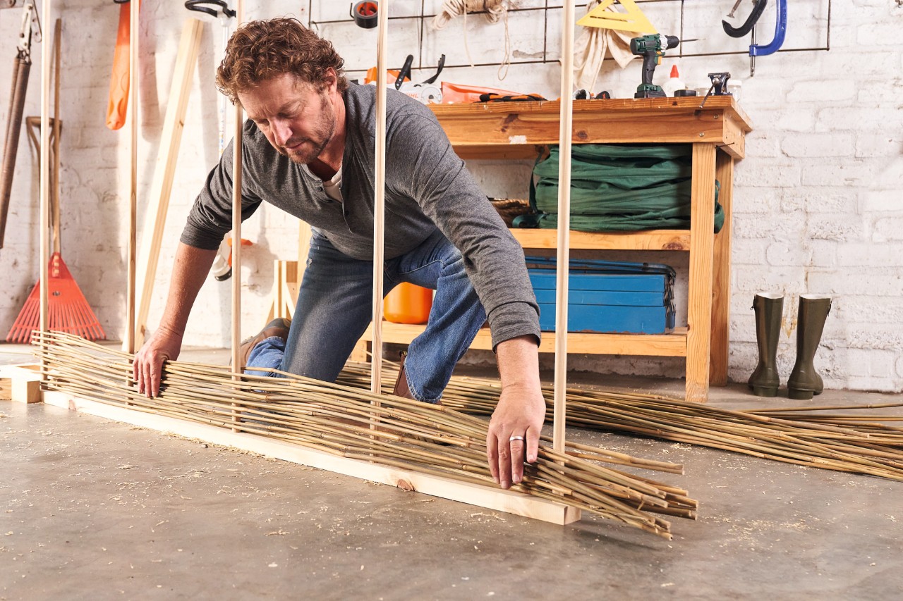 A man weaving bamboo canes for a DIY privacy screen