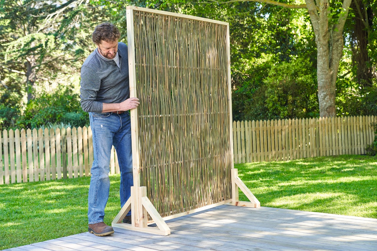 A man setting up a DIY garden screen on his wooden terrace