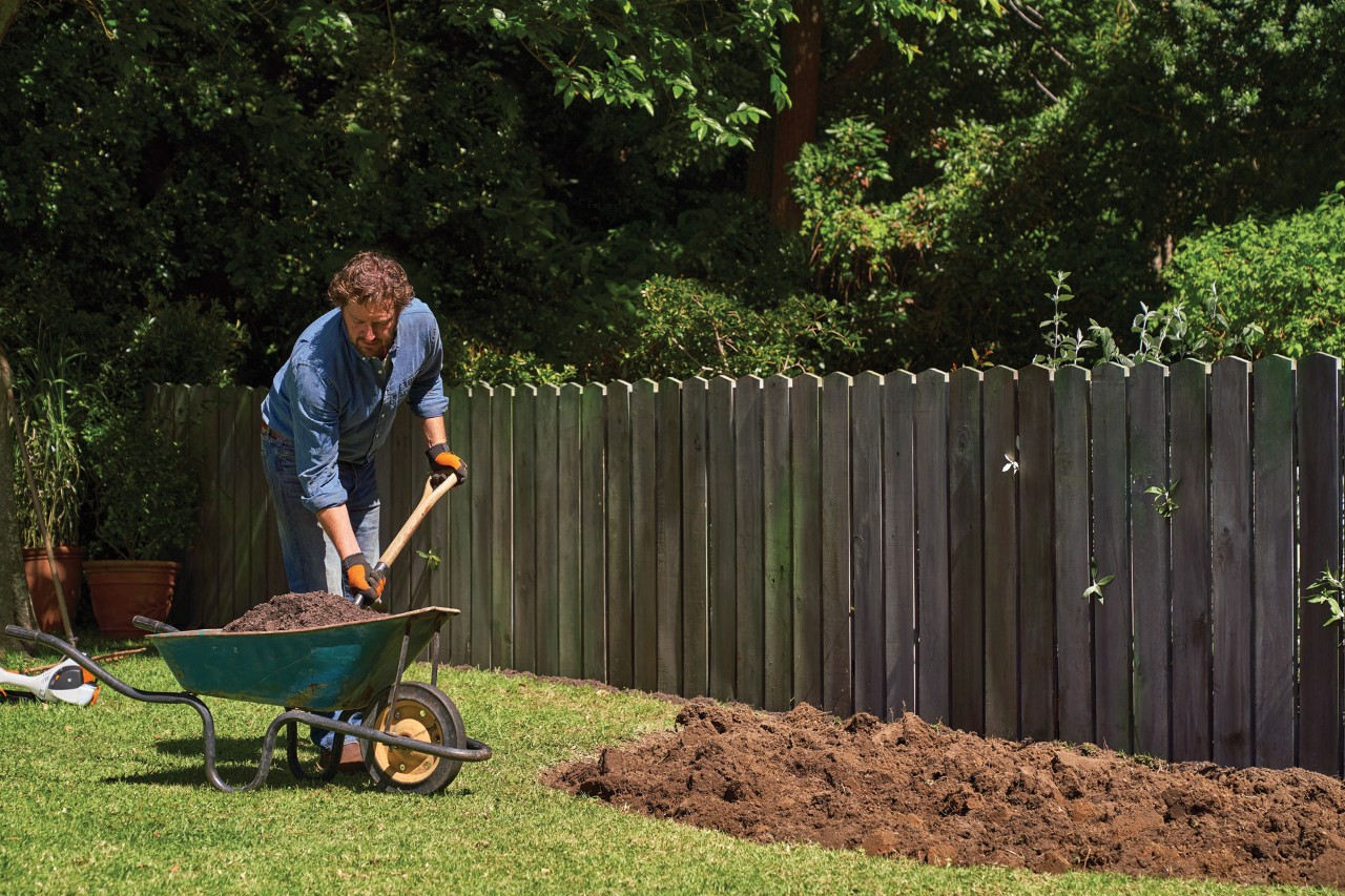 A man shovelling compost from a wheelbarrow into a bed of bare earth