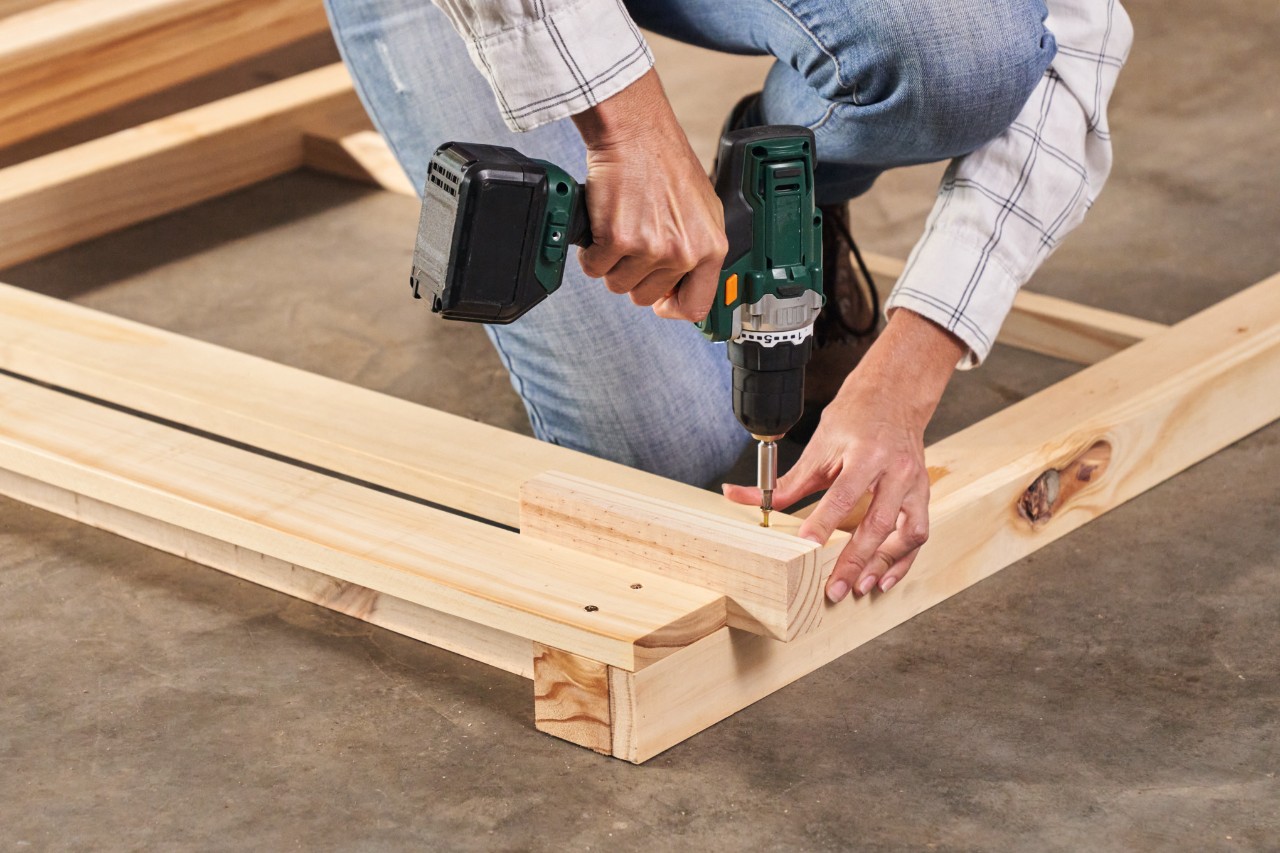 Close-up of a person using a cordless screwdriver to bolt wooden slats together for a DIY composter 