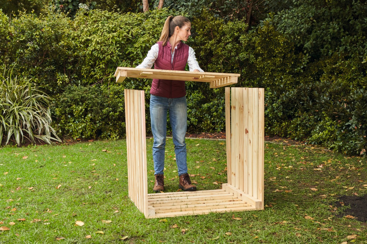 Woman on a garden plot precisely positioning the front of the DIY composter on the projecting side walls