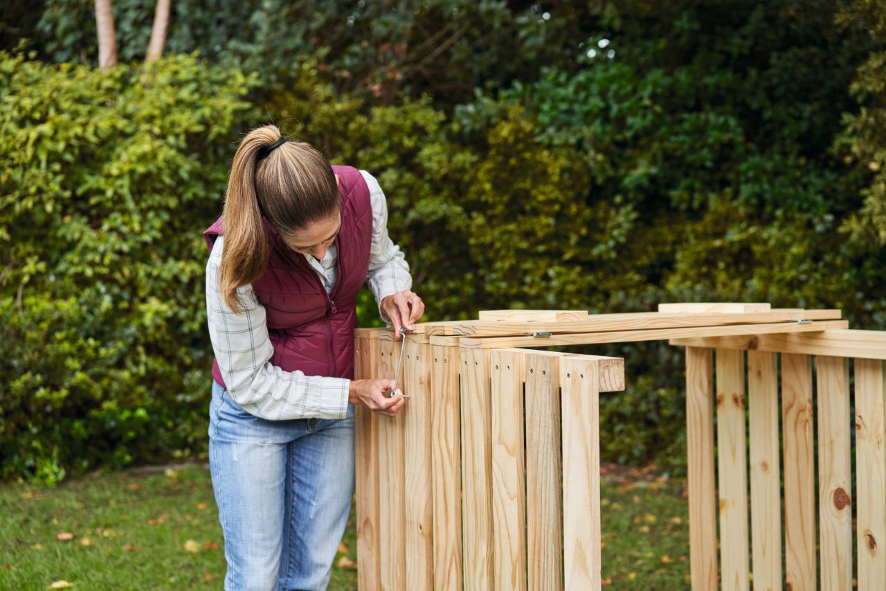Woman attaching cabin hooks to a DIY composter on a garden plot 