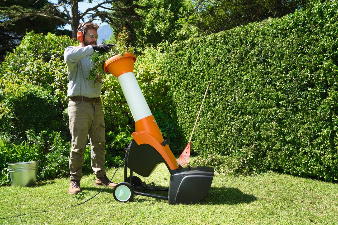 A man wearing ear protection shreds hedge trimmings