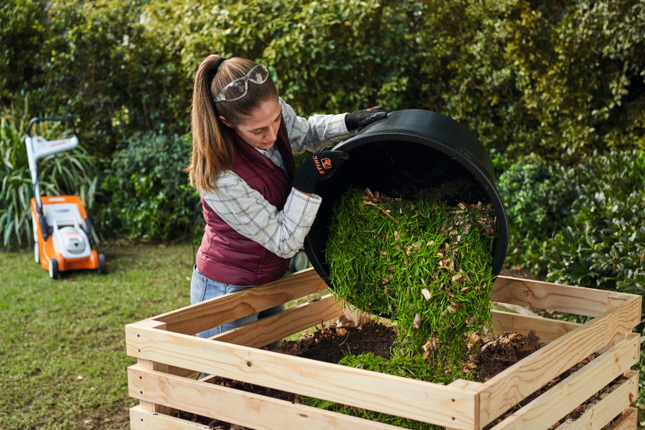 Woman is emptying the bucket filled with lawn grass cuttings and shredded branches