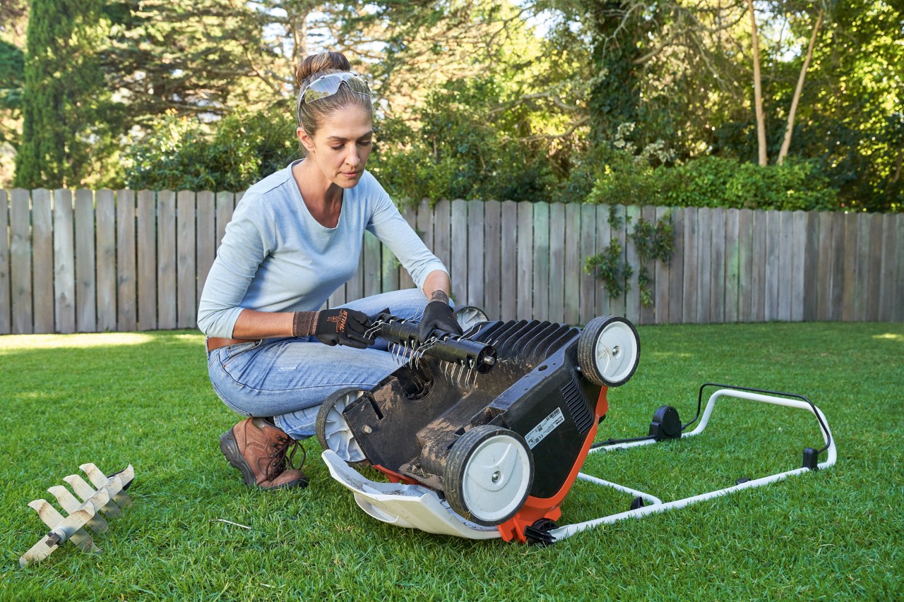 Woman wearing eye protection and work gloves replacing the scarifying unit of the STIHL RLA 240 cordless lawn aerator.