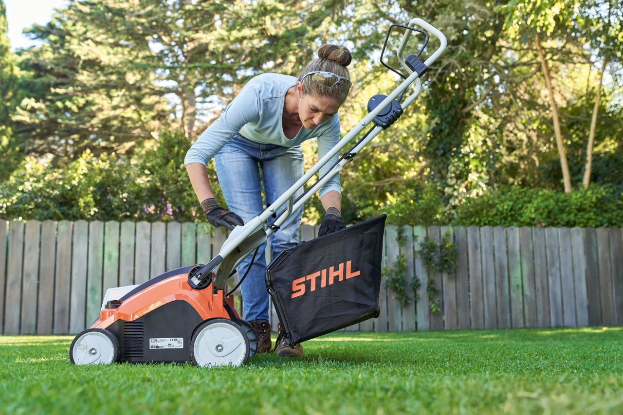 Woman securing the collection box of the STIHL RLA 240 cordless lawn scarifier to the rear of the power tool.