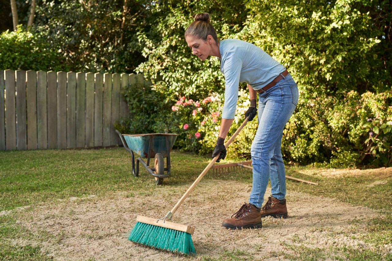 A woman with a broom in her hand sanding a lawn