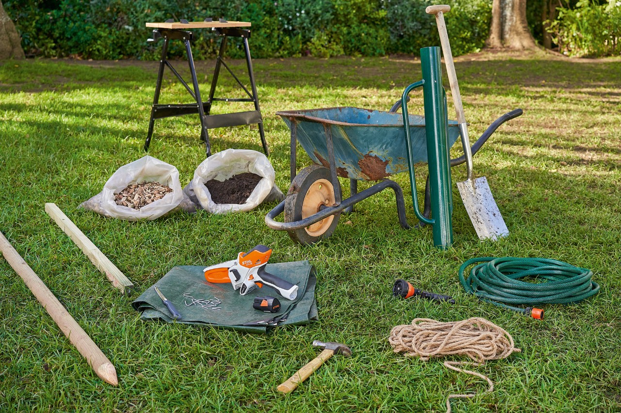 Working materials for tree planting lying on a lawn, including the STIHL GTA 26 cordless garden pruner.