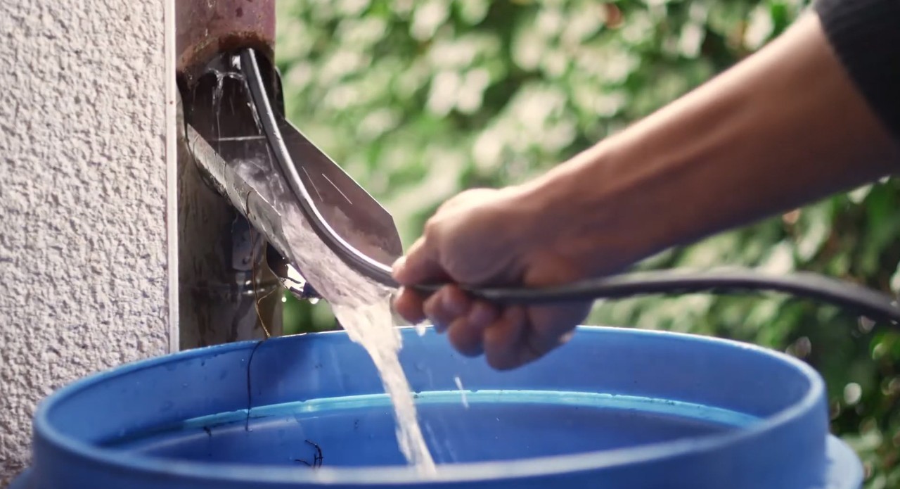 A flexible metal rod is pushed into a downpipe to clean the blocked inlet into a blue water butt