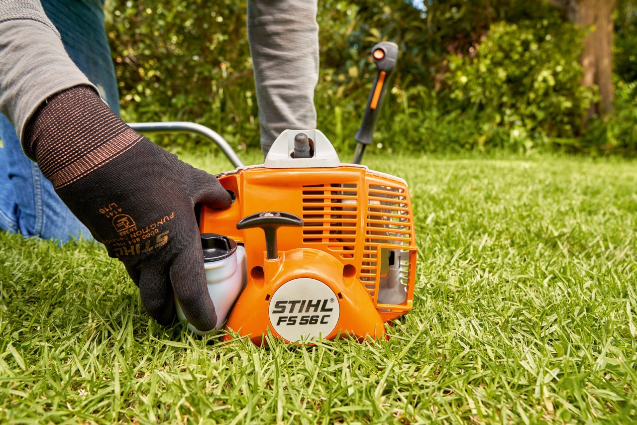 A man pressing the fuel pump of a STIHL FS 56 petrol brushcutter to start it
