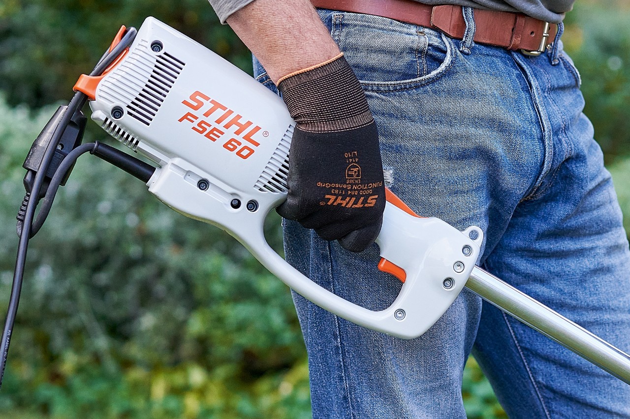 Man pressing switch to switch off the STIHL FSE 60 electric brushcutter.