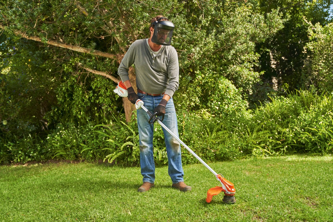 A man wearing face protection mowing grass in a garden using the STIHL FSA 60 cordless brushcutter