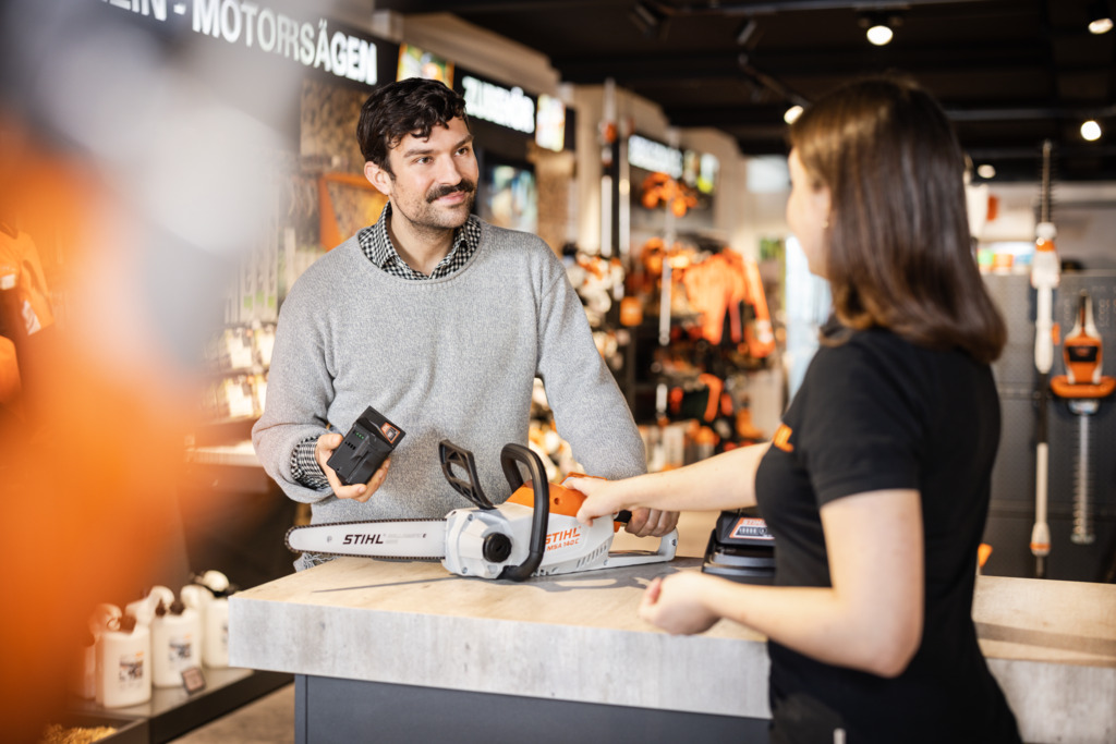 STIHL dealer advising a young woman about a STIHL hedge trimmer in front of a store shelf