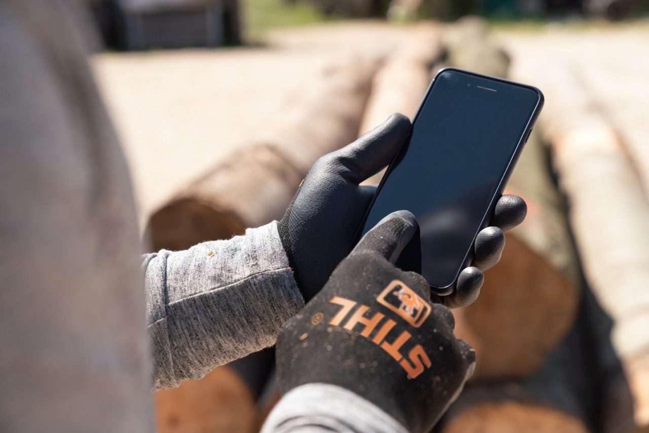 A man wearing STIHL protective gloves taps his smartphone