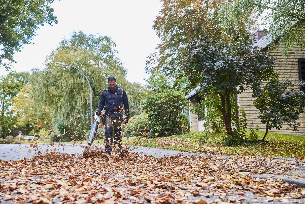 A gardener and landscaper removing leaves from a road using a STIHL BGA 200 cordless blower.