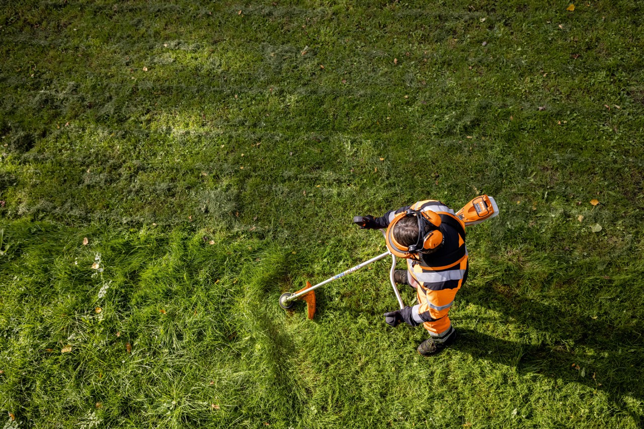A gardener and landscaper in orange work clothes mowing tall grass using a STIHL FSA 135 cordless clearing saw