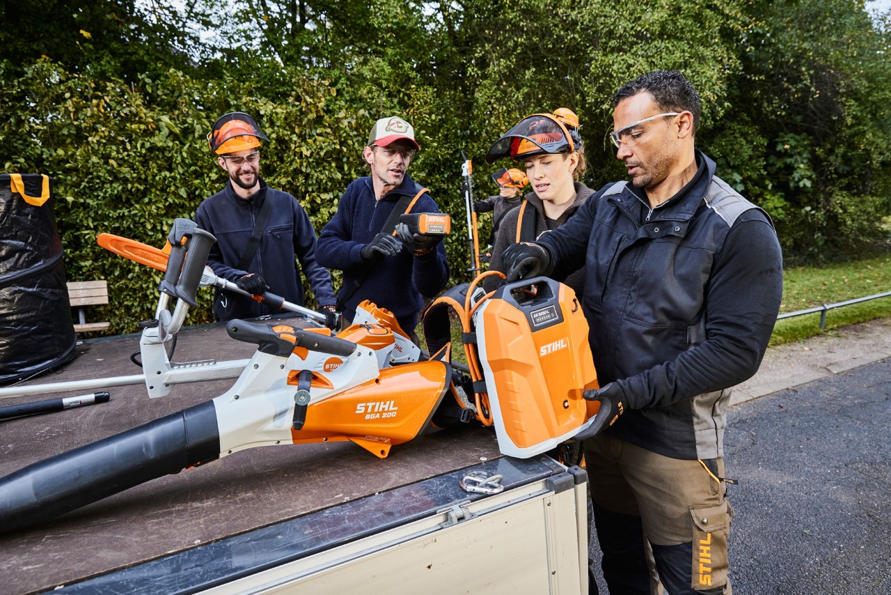 Gardeners and landscapers taking STIHL AP-System power tools and a backpack battery from their vehicle’s loading area.
