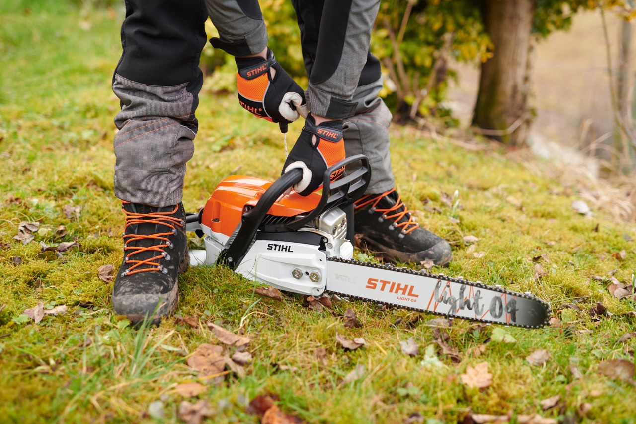 A STIHL MS 261 C-M petrol chainsaw being started on the ground